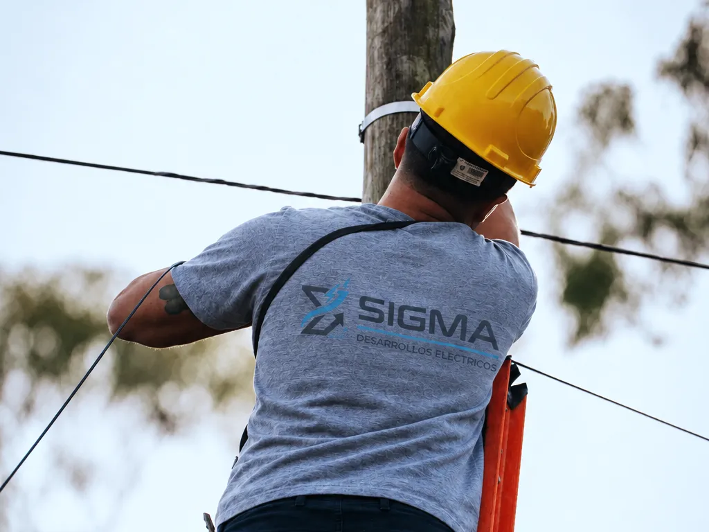 Técnico de Sigma con casco y escalera trabajando en el tendido de un poste de madera