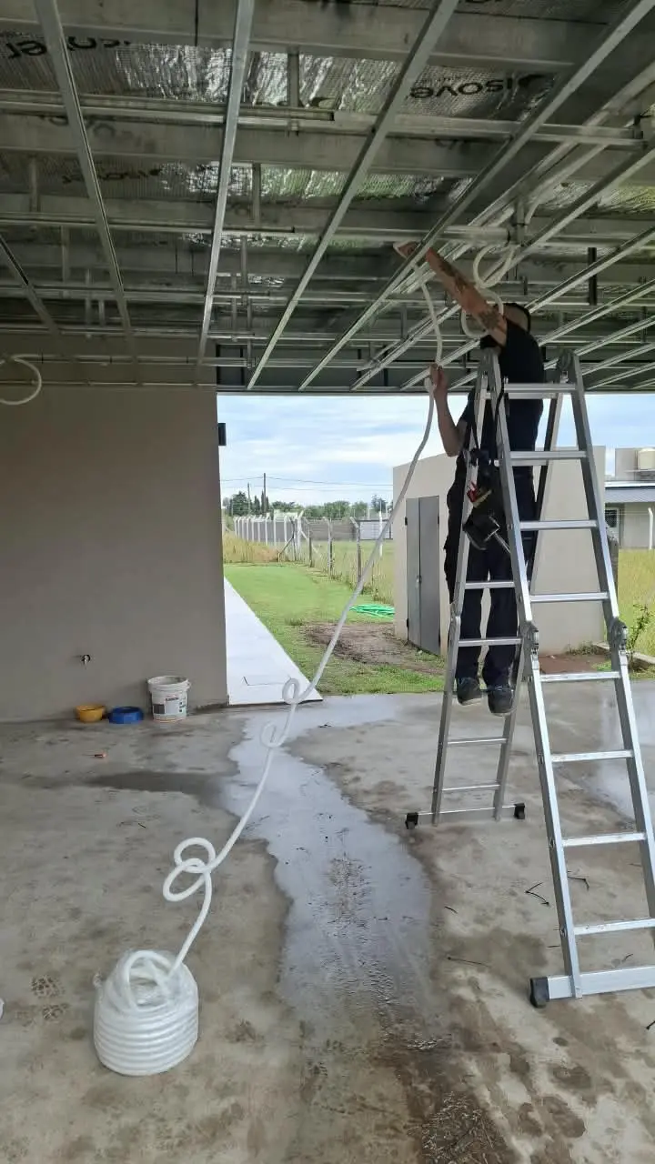 Electricista de Sigma sobre una escalera pasando cables por la estructura del techo