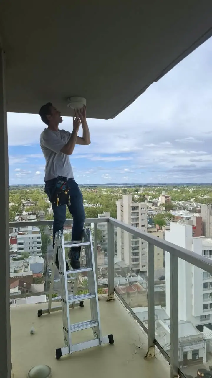 Electricista sobre la escalera trabajando en la iluminación del balcón