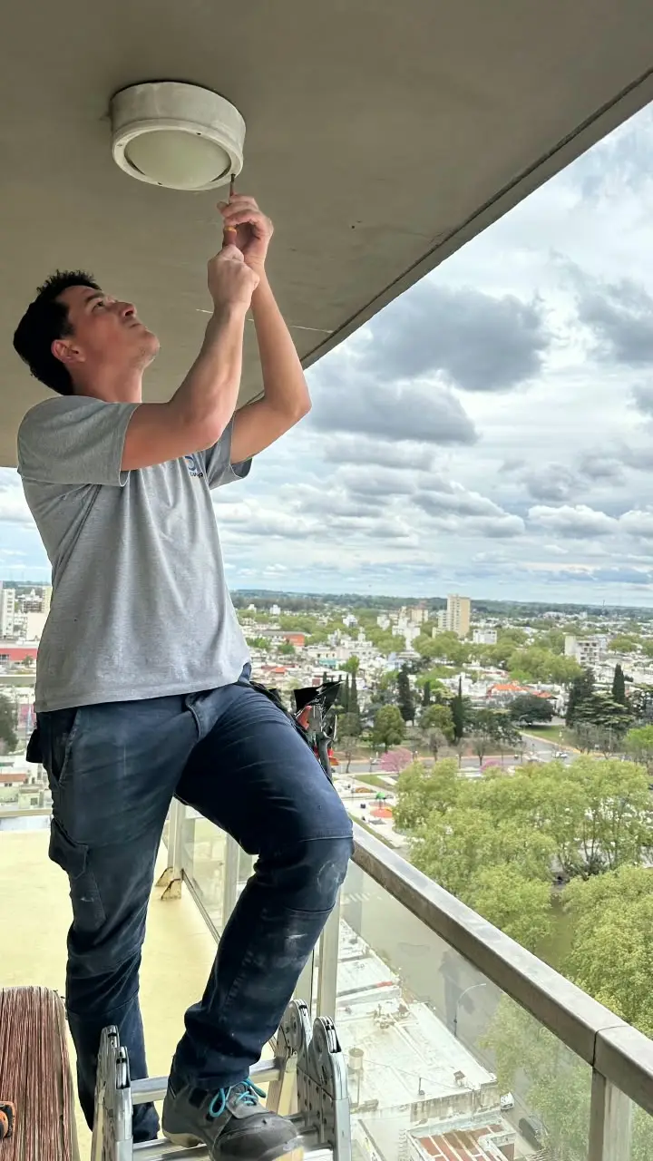 Electricista revisando un plafón del balcón, con la ciudad de fondo